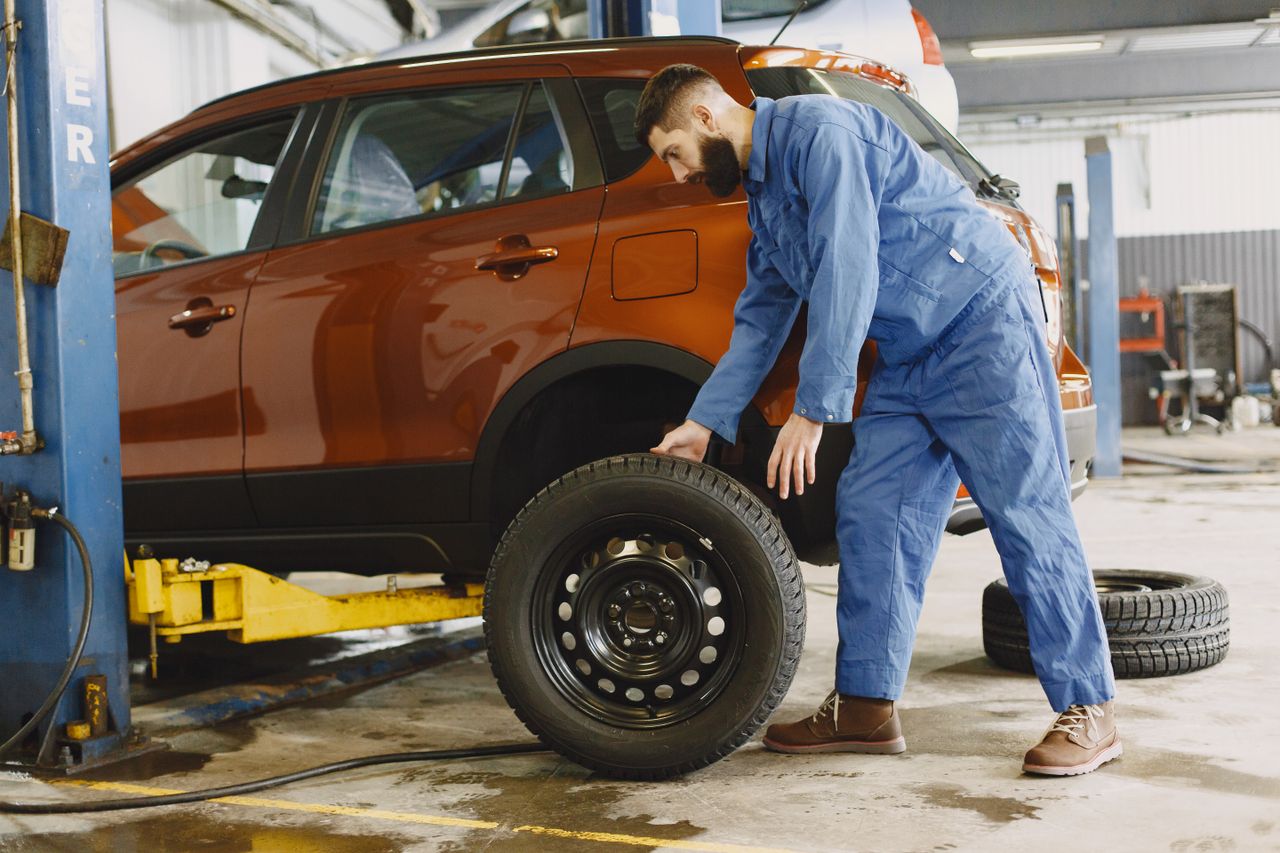 Crafting Captivating Headlines: Your awesome post title goes here Mechanic in blue coveralls replacing tire on red SUV in repair shop garage.